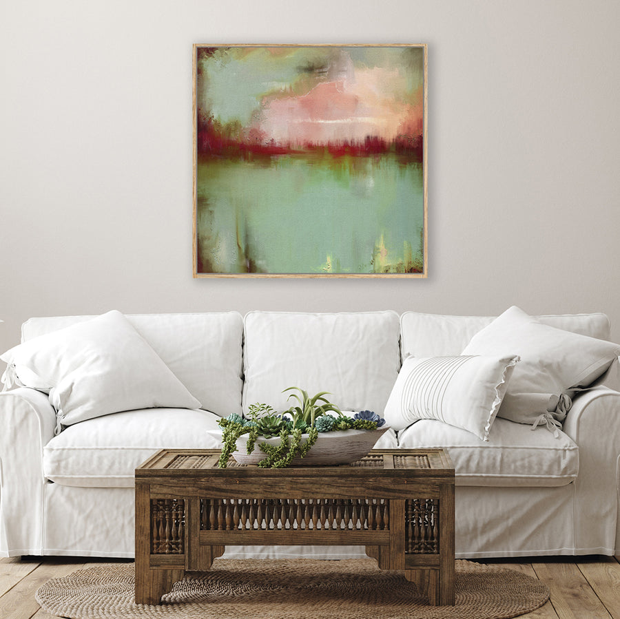 Abstract canvas art print of a sage green lake and crimson sunset, displayed above a white linen couch in a country-style living room.