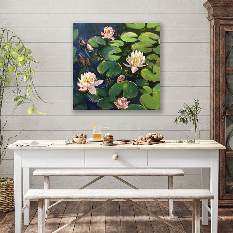 Wall art print of green lily pads and pink lilies floating on dark pond water displayed behind a rustic farmhouse dining table.