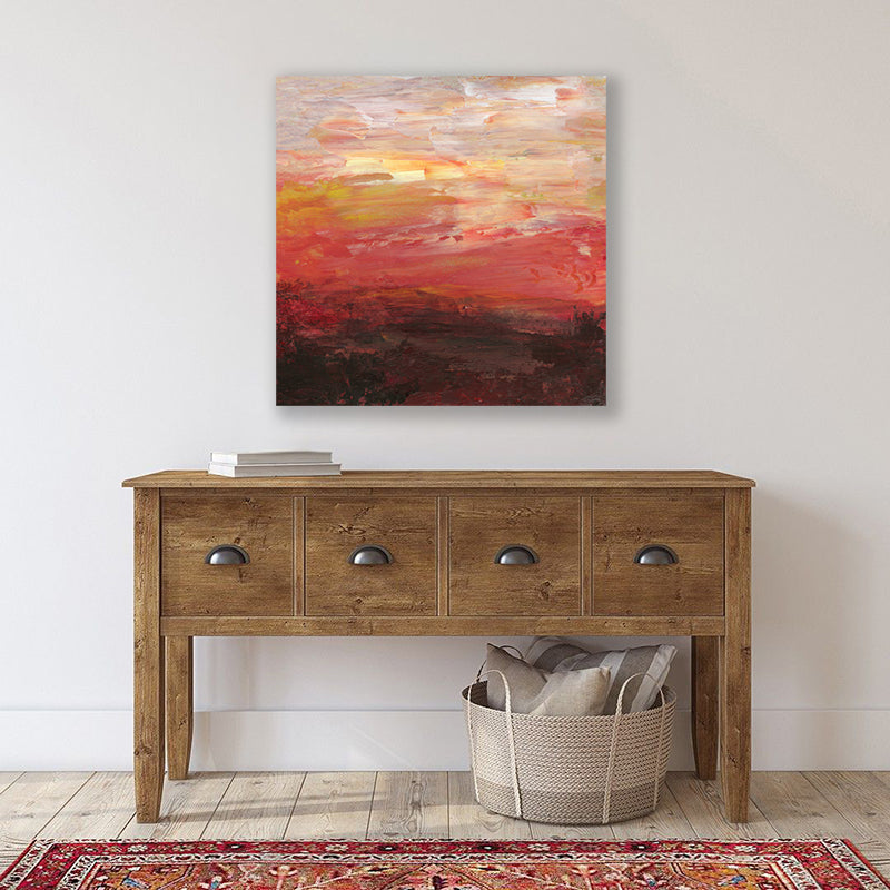 An abstract canvas wall art print featuring a fiery brick-red sunset above a deep mahogany outback landscape, displayed on a wall above a wooden console table with a red Persian rug in front.