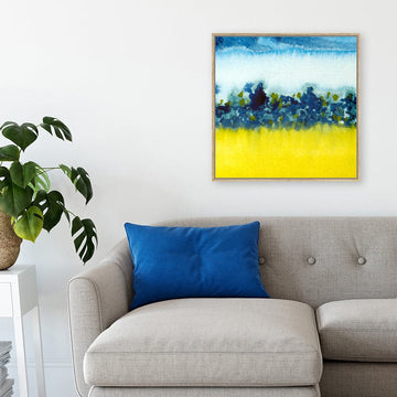 Blue and yellow abstract landscape canvas art print above grey sofa with bright blue cushion in modern interior.  