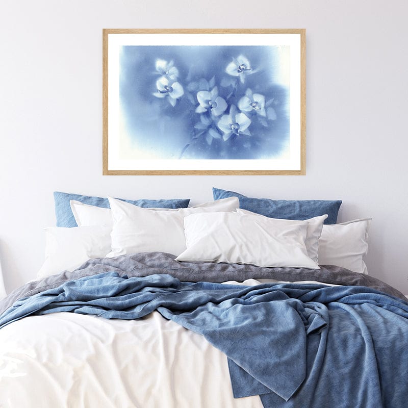 Framed watercolour fine art print of white orchids set against a denim blue afternoon sky in a white and blue bedroom.